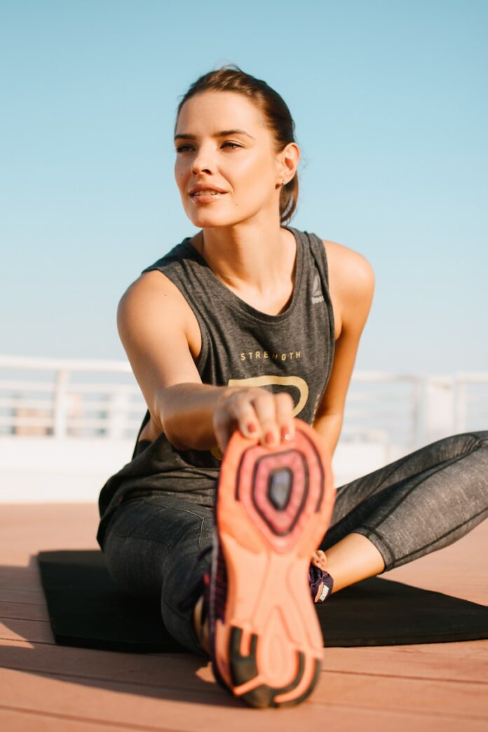 Photo by Christina Moroz woman in black tank top and blue denim jeans sitting on brown wooden bench during daytime