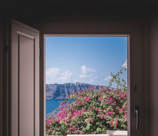 더위를 이기는 집안 관리법 opened window showing outdoor lounger and pink flowers with mountain background