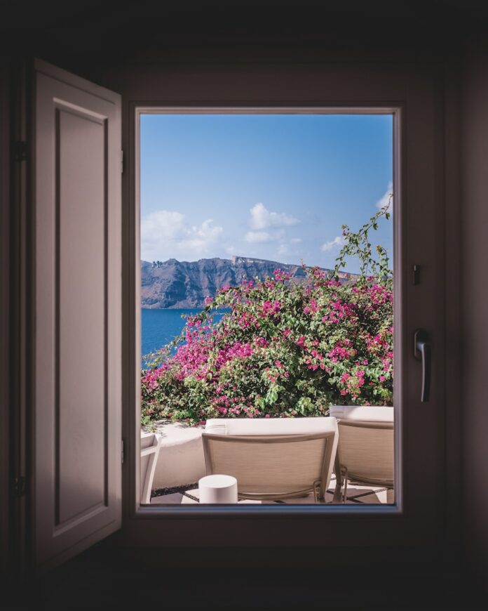 Photo by Cosmic Timetraveler opened window showing outdoor lounger and pink flowers with mountain background