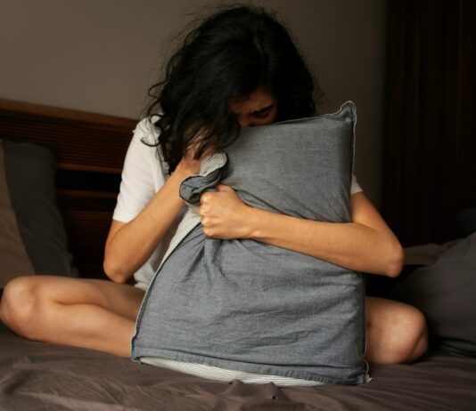 현대인의 불면증: 원인과 해결책 A woman sitting on a bed holding a pillow