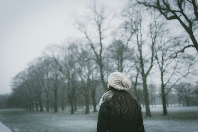 Photo by Paul Green woman wearing cap and black coat standing near bare tree