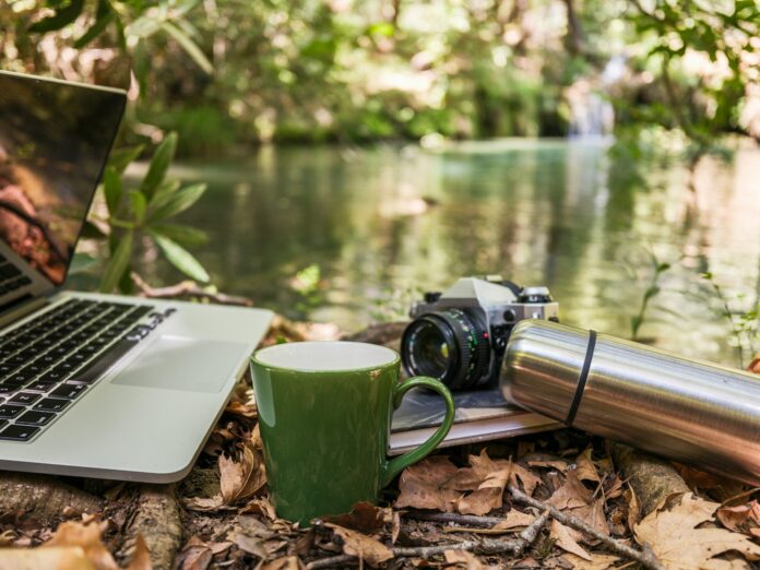 Photo by engin akyurt Laptop, camera, and mug by a forest stream