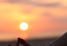 “마음챙김 명상, 바쁜 일상 속 스트레스 해소법으로 주목” A person sitting in a yoga position with the sun setting in the background